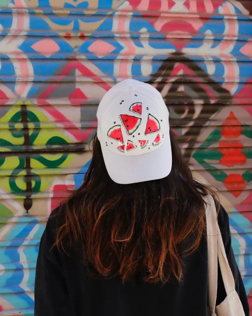 Person with a watermelon cap facing a vibrant geometric graffiti wall