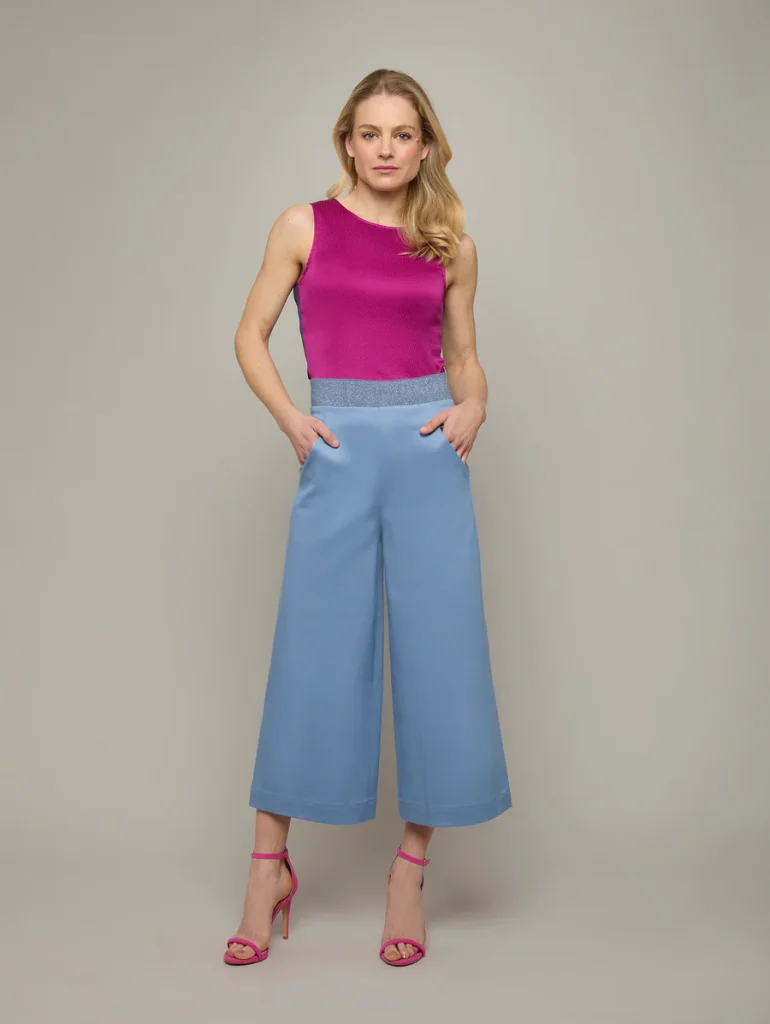 Woman models chic sleeveless pink top and blue wide-leg pants with matching pink heels against a neutral background