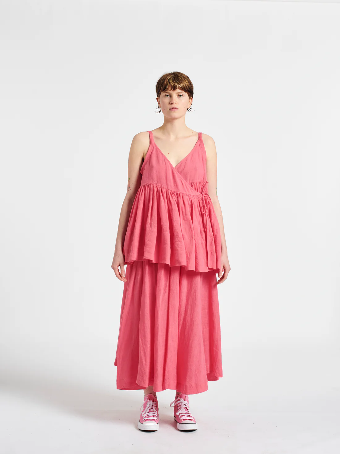 Person wearing a pink dress and sneakers, standing against a white background. Fashion style and outfit inspiration