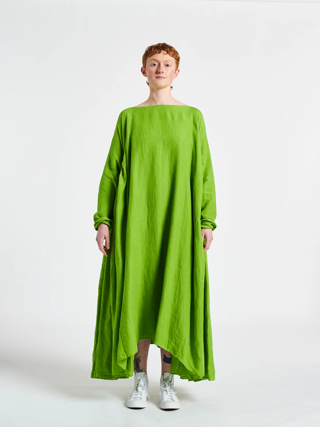 Person wearing a flowing green dress and white sneakers, standing against a plain background