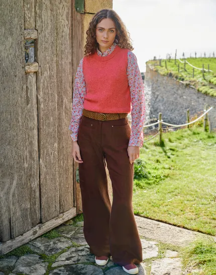 Woman in a vintage outfit stands outdoors by a rustic wooden door on a sunny day