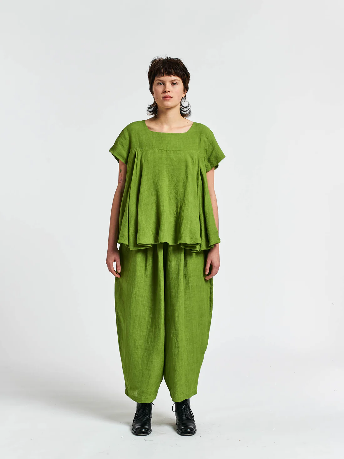 Woman in a green two-piece linen outfit with loose pants and top, standing against a white background