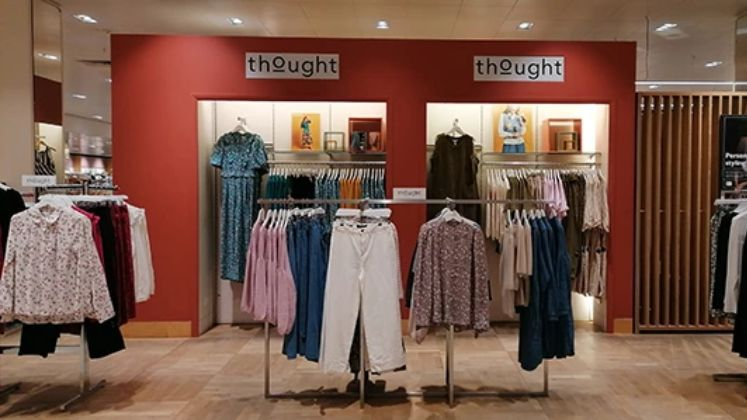 Clothing store interior with racks of colorful women's clothes and a red wall with thought signage.