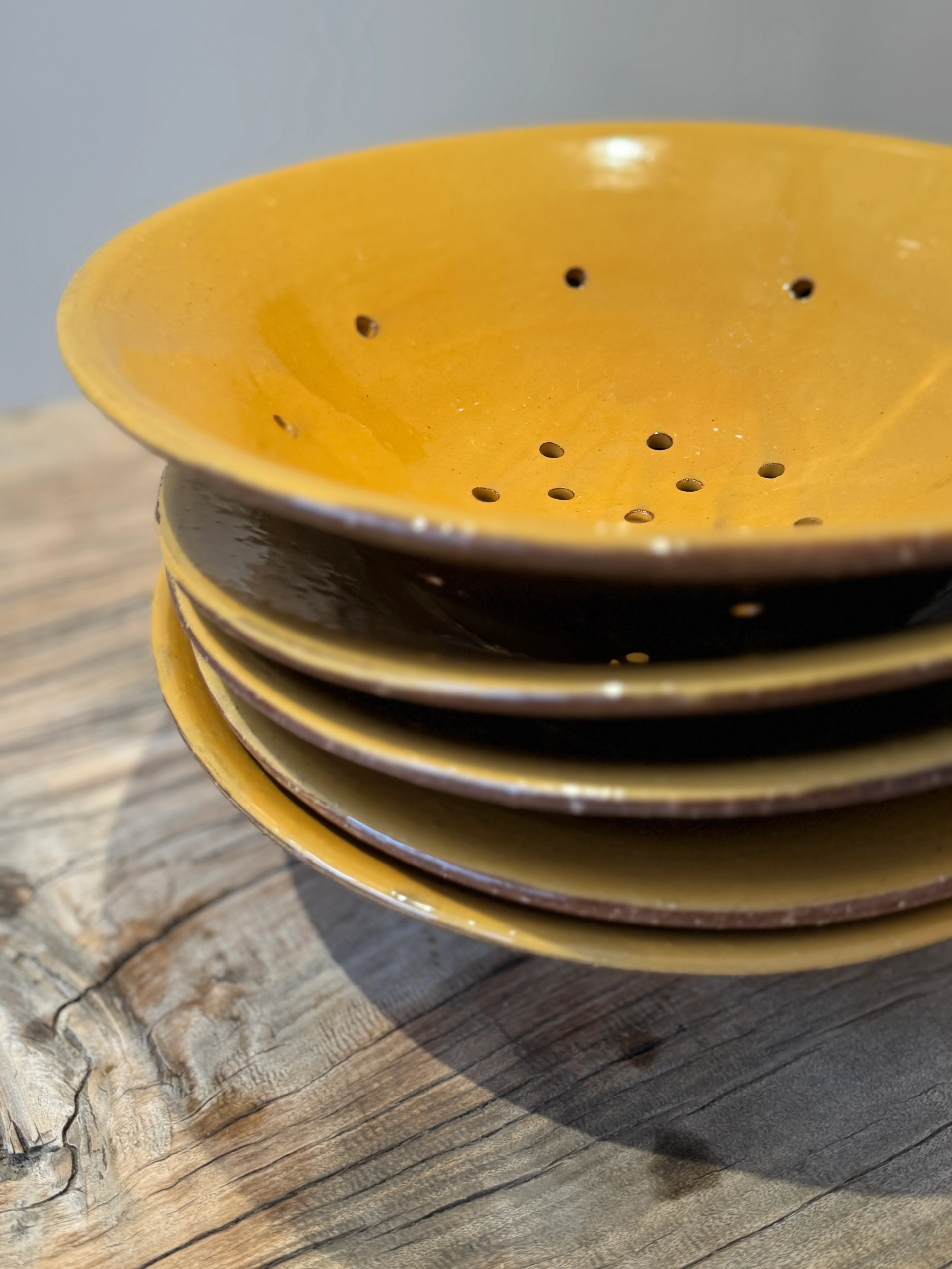 Stack of rustic yellow ceramic plates with holes on a wooden table. Perfect for kitchen decor or serving.