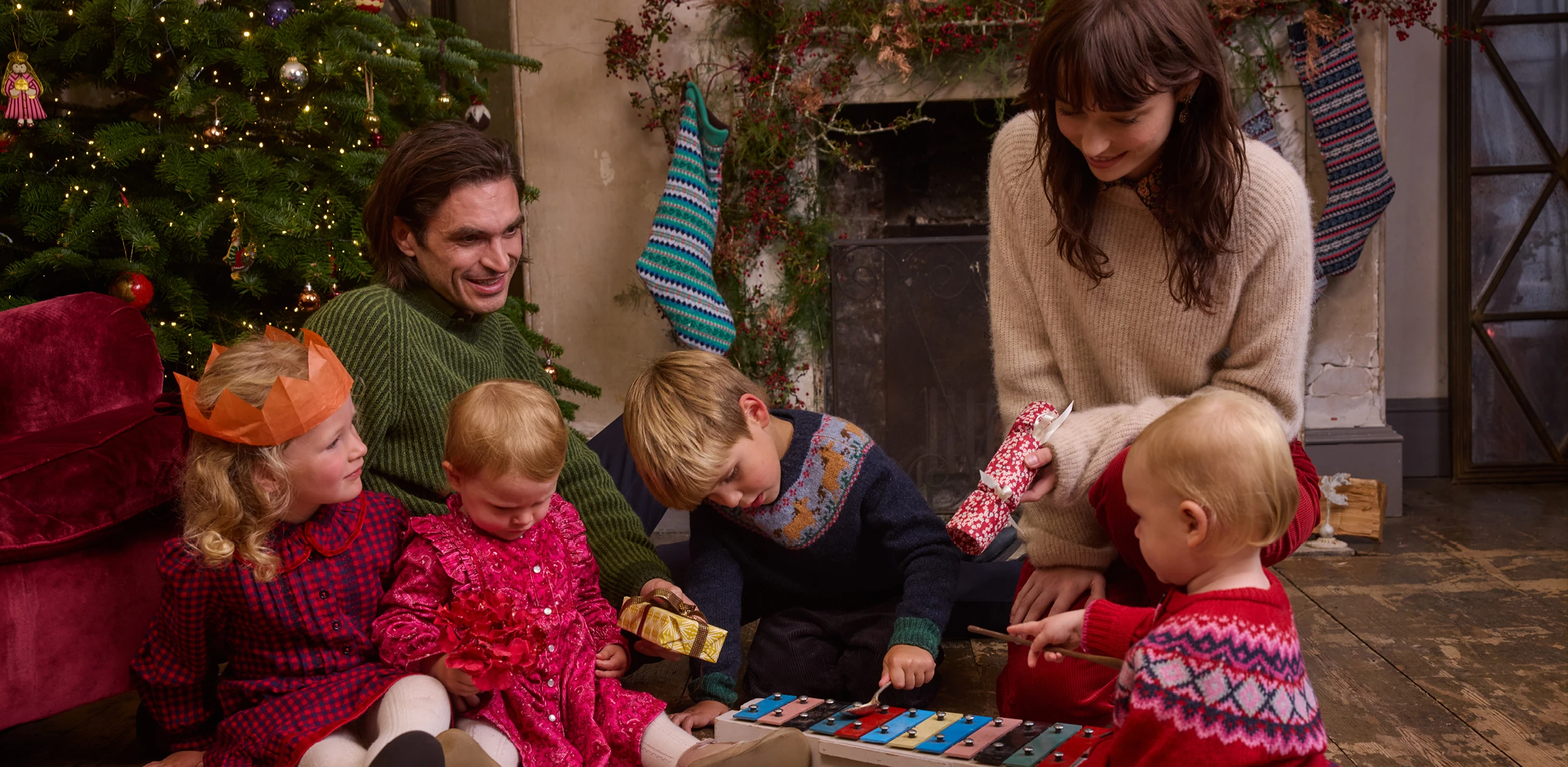 Family enjoying Christmas together, with children playing in front of a decorated tree and festive stockings