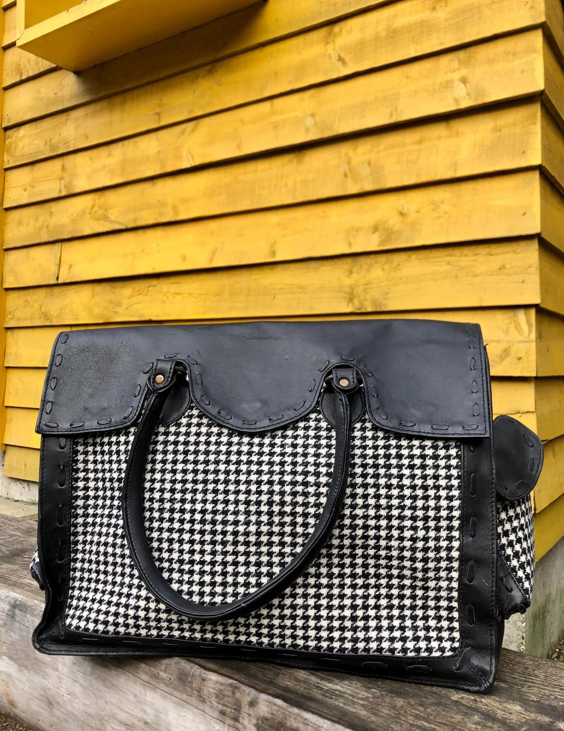 Black and white houndstooth handbag on wooden bench, yellow wooden wall background.