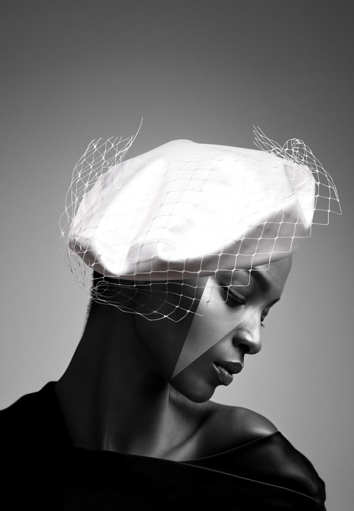 Elegant woman wearing a stylish netted hat, gazing down in black and white photography