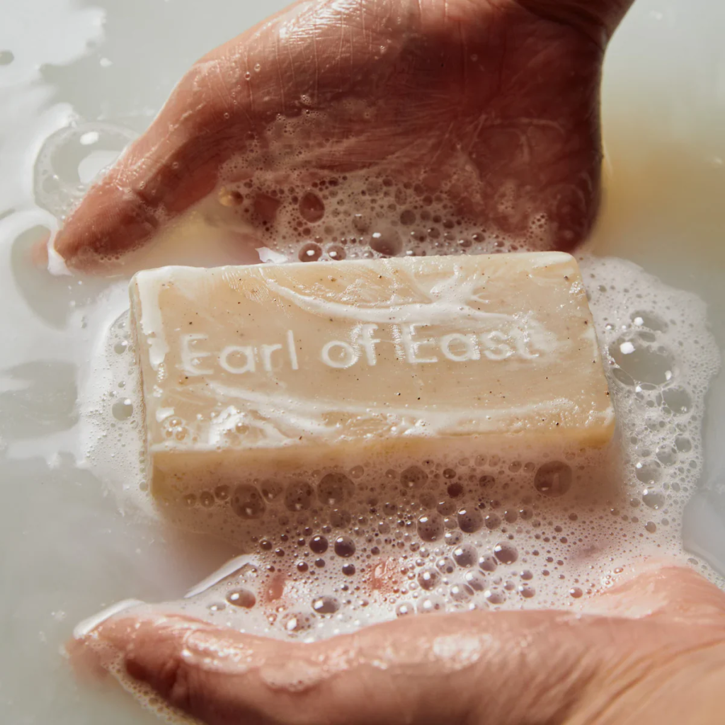 Hands holding a bar of Earl of East soap in foamy water