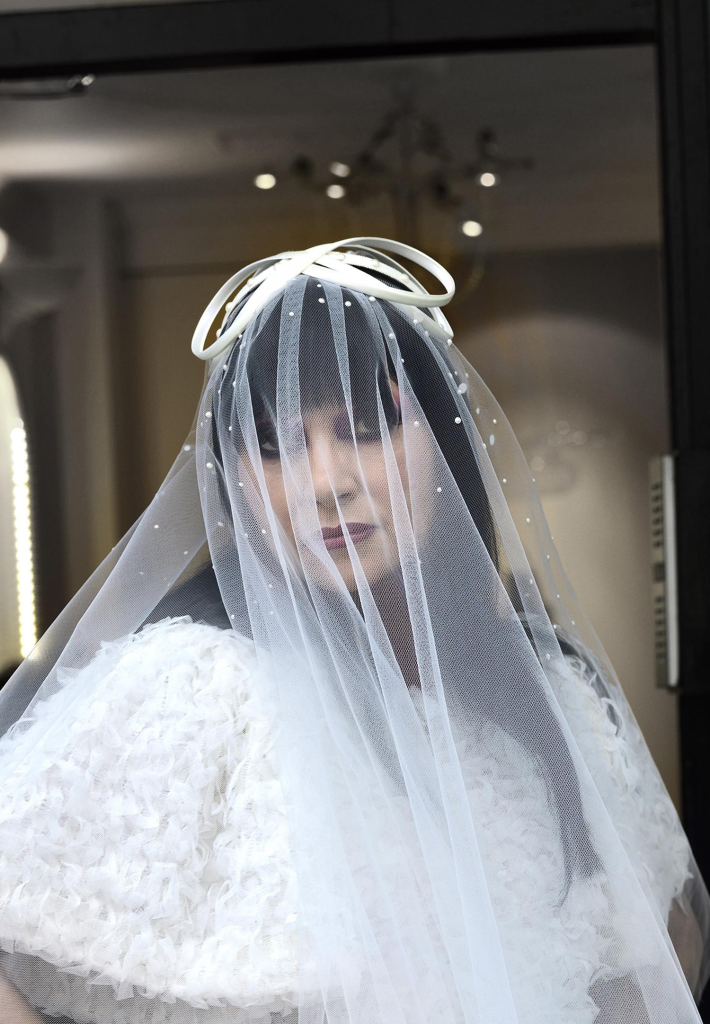 Elegant woman in a unique, artistic bridal outfit with a sheer, embellished veil and bow headpiece