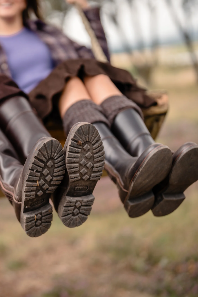 Two people in boots swinging outdoors, focus on worn boot soles with nature background.