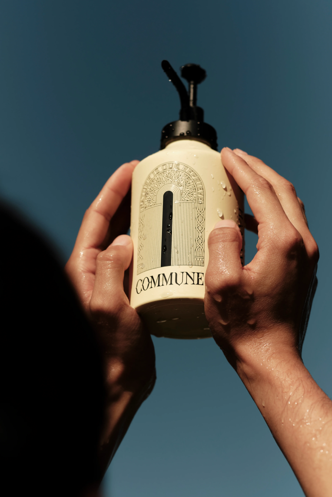Hands holding a bottle of Commune soap against a clear sky background