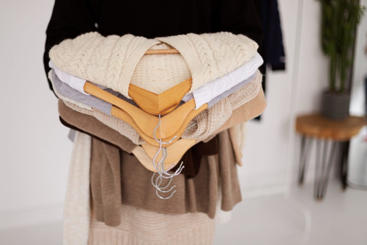 Pile of cosy knitted sweaters in neutral tones stacked on wooden hangers for autumn wardrobe organisation