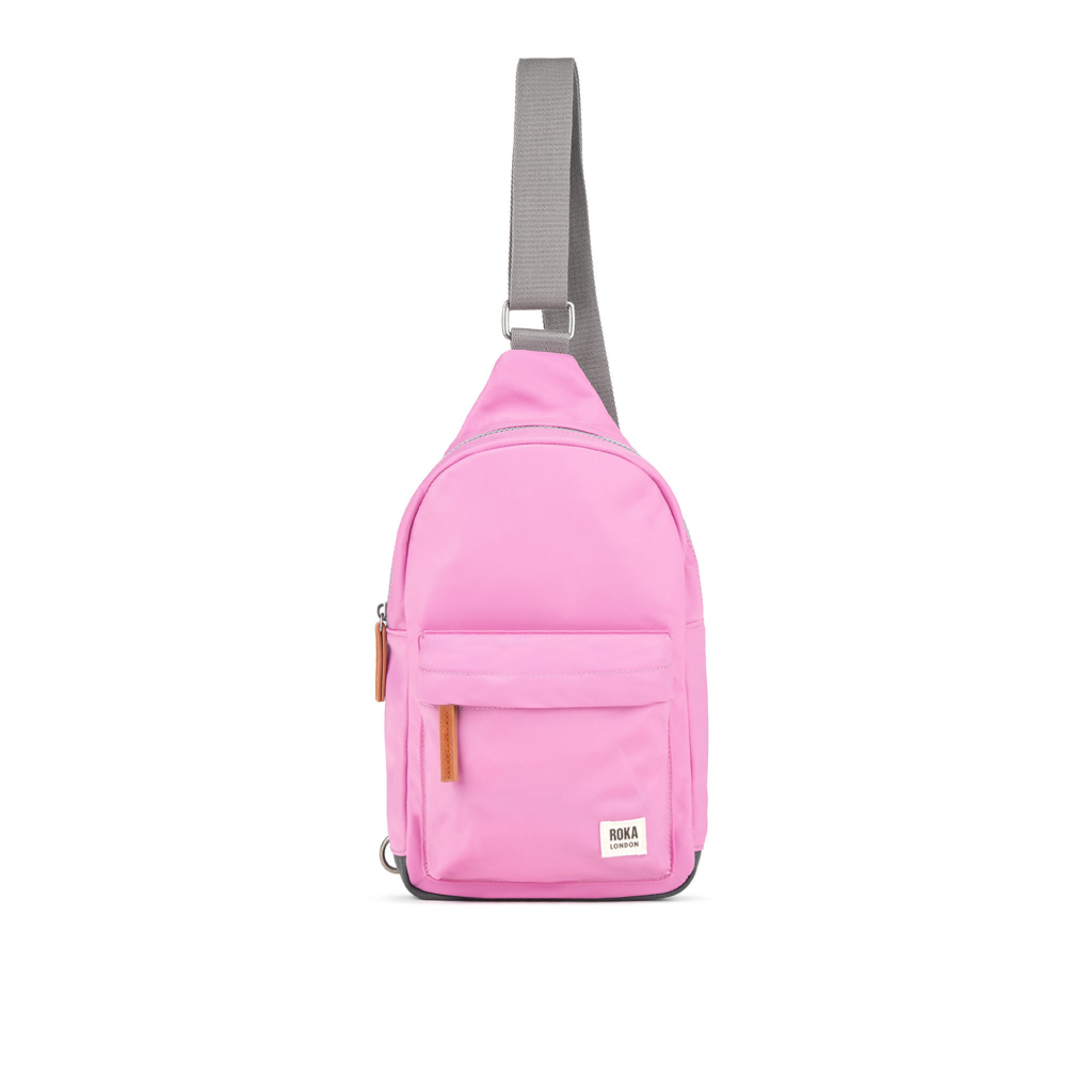 Pink sling backpack with a front pocket and gray strap, suitable for casual wear and travel.