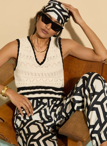 Fashion-forward woman in black and white geometric outfit with sunglasses and headscarf, sitting relaxed.