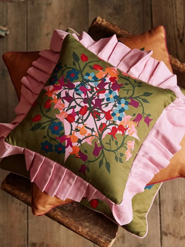 Floral cushion with pink ruffles on rustic wooden chair, colorful embroidered design.
