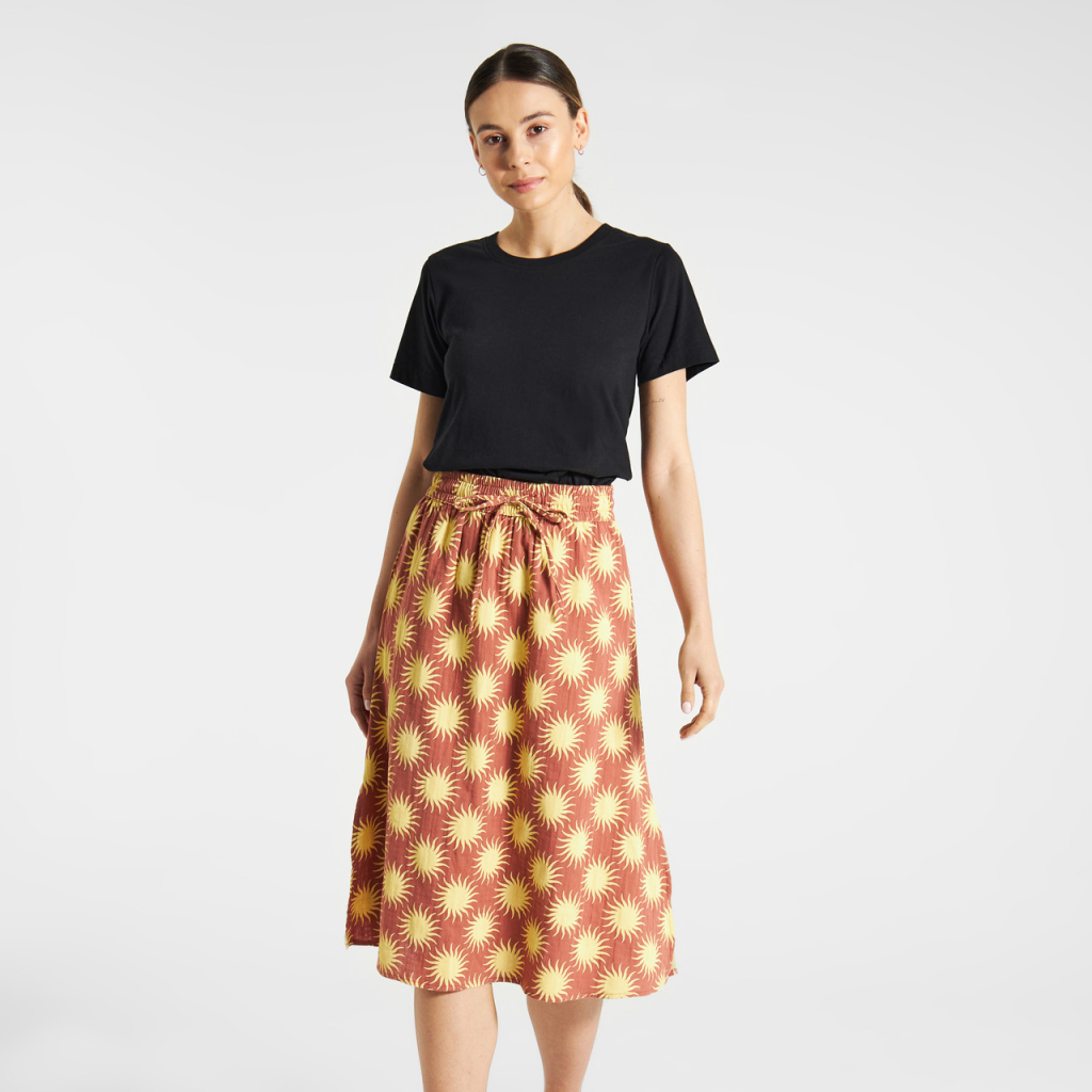 Woman in black T-shirt and sunflower-patterned skirt against a plain background.