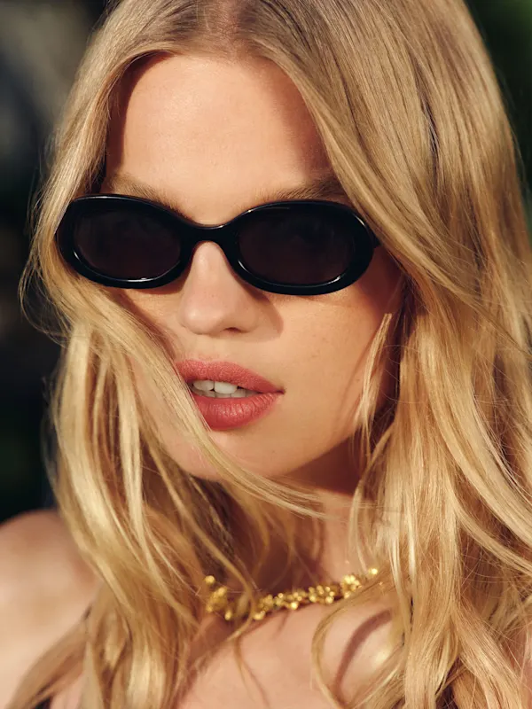 Woman with blonde hair wearing black sunglasses and a gold necklace.