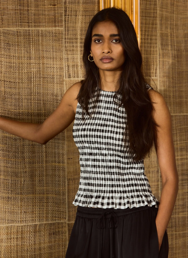 Woman in black and white checkered top poses against textured background.